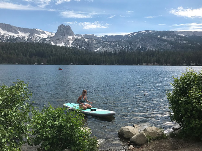 Woman in paddle boat on the lake with mountains behind.