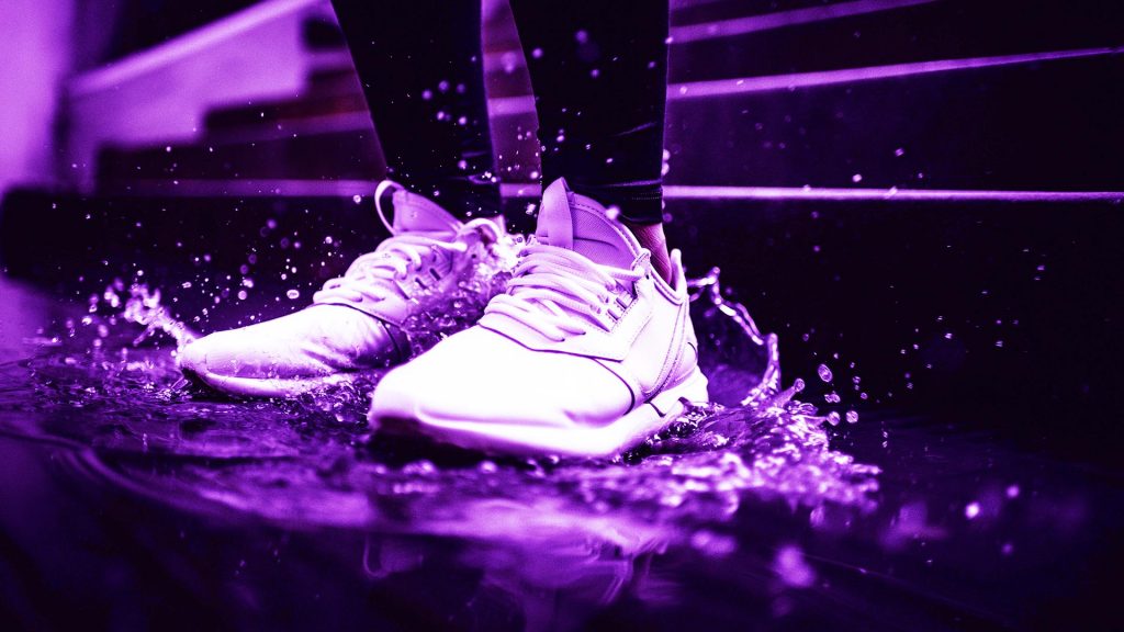 closeup of white tennis shoes splashing in puddle.