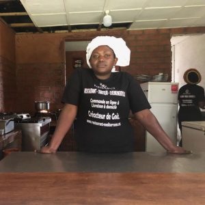 One of the teen mom students standing in a chef's hat at the counter of the class restaurant.