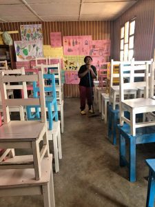 Teen mom standing in the cleaned classroom. Chairs stacked on top of the desks.