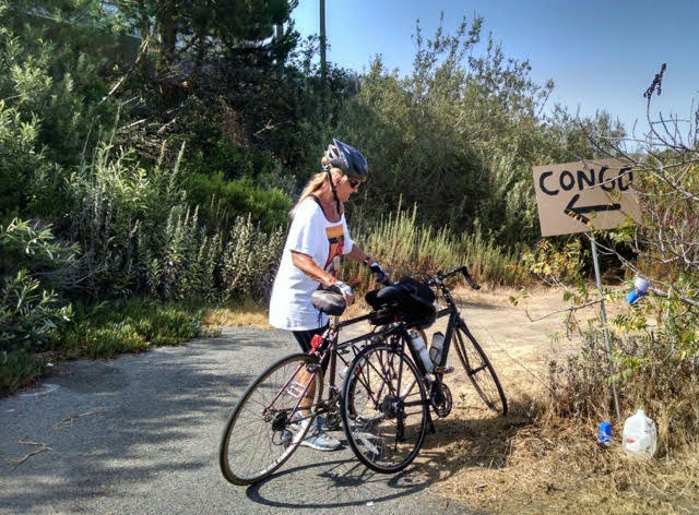 Anastasia with her bicycle and a sign with an arrow point to Congo.