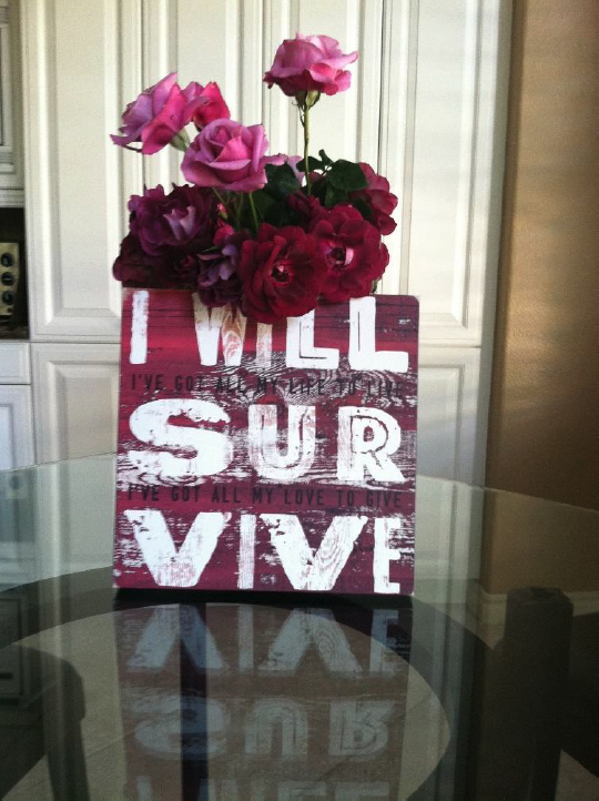 Flowers and a sign on a table, sign says, I will survive.
